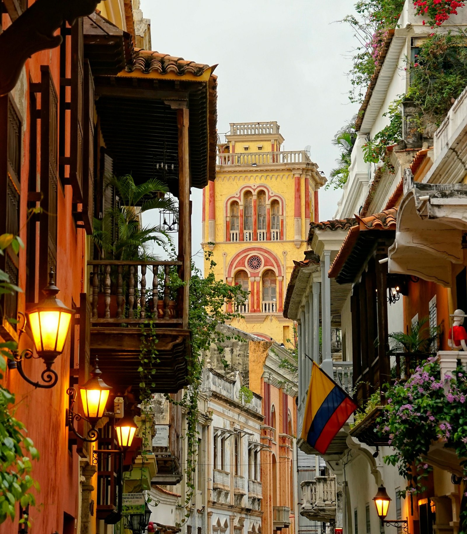 Calle colonial angosta en Cartagena, Colombia, con edificios de colores y una torre de iglesia amarilla